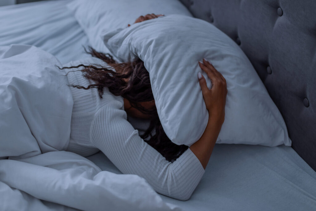 stressed-black-woman-covering-head-under-pillow-ly-2023-11-27-05-12-12-utc-scaled.jpg