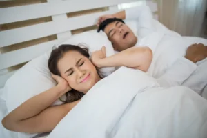 portrait_woman_blocking_ears_with_man_sleeping_snoring_bed_1.webp.webp